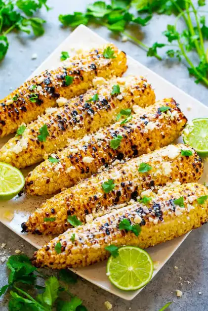 Corn On The Cob Mexican Style Corn On The Cob Mexican Style A white platter of grilled corn on the cob Mexican style, topped with crumbled cotija cheese, fresh cilantro, and served with lime wedges.