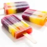 Three healthy rainbow popsicles with a vibrant dragon fruit layer, arranged on a clean white surface.