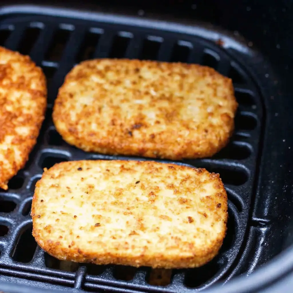 Close-up of crispy, goldentrader joes hashbrown air fryer patties cooking in a single layer inside a black air fryer basket.